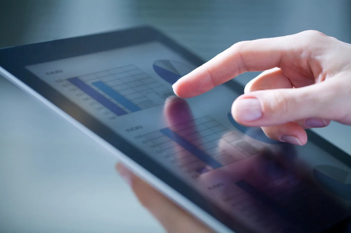A hand touching a tablet showing bar charts.